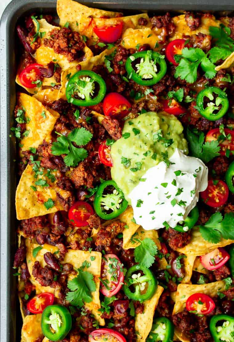 Close up of sheet pan restaurant style nachos with a dollop of sour cream and a dollop of guacamole in the middle