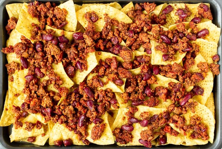 Tortilla chips on a sheet pan topped with vegetarian chili.