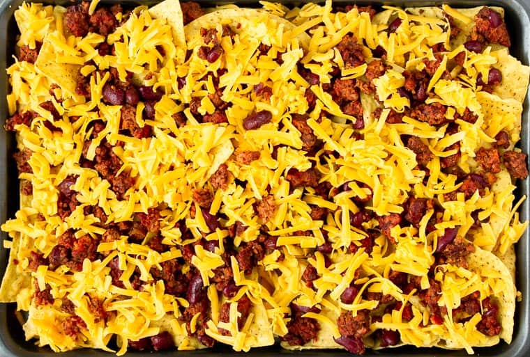 Tortilla chips on a sheet pan topped with vegetarian chili and cheese