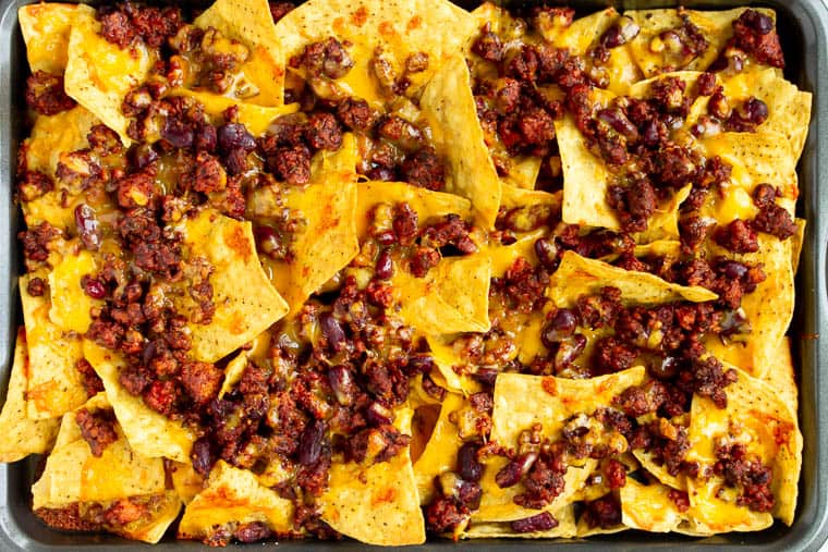 Baked tortilla chips on a sheet pan topped with vegetarian chili and melted cheese