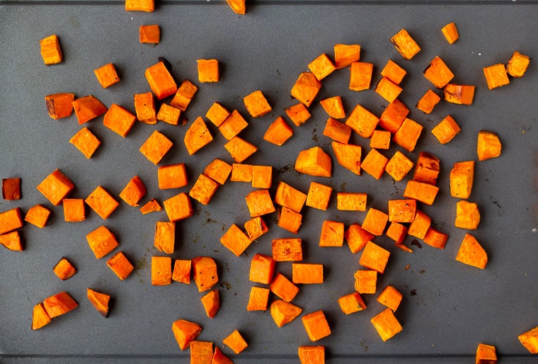 Roasted diced sweet potatoes on a gray sheet pan