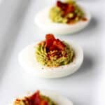 Three bacon avocado deviled eggs on a white serving plate.