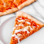 A slice of buffalo chicken pizza drizzle with ranch dressing on a white plate with text overlay.
