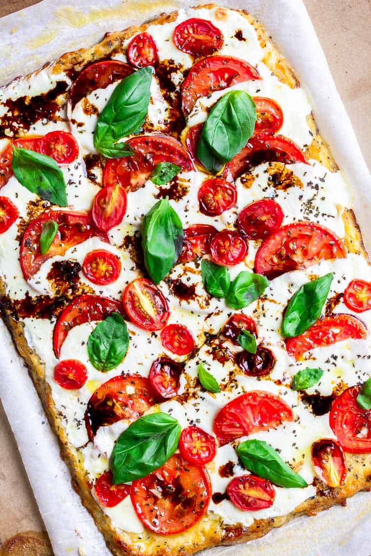 Caprese Pizza on a pizza stone with parchment paper under it