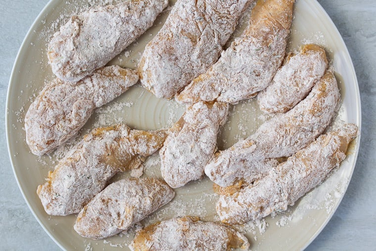 Floured chicken tenders on a white plate