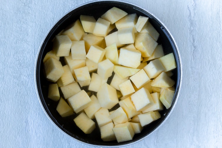 Cubes of rutabaga in a black saucepan over water over a white background