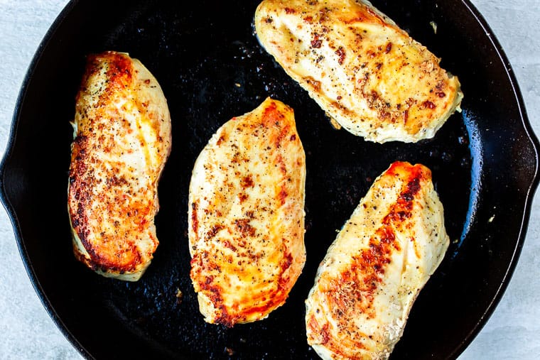 4 Chicken breasts cooking in a cast iron skillet over a white background