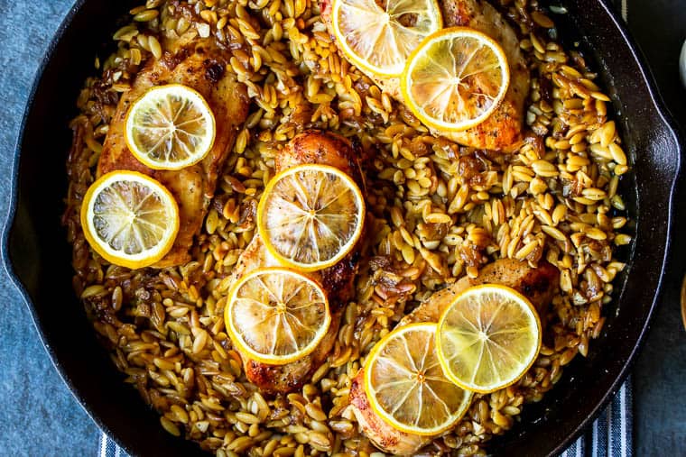 Baked Lemon Garlic Chicken with Orzo Pasta in a cast iron skillet on a blue and white striped towel over a blue background