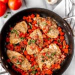 Bruschetta chicken in a black skillet with tomatoes, garlic, basil and bread crumbs around it with text overlay.