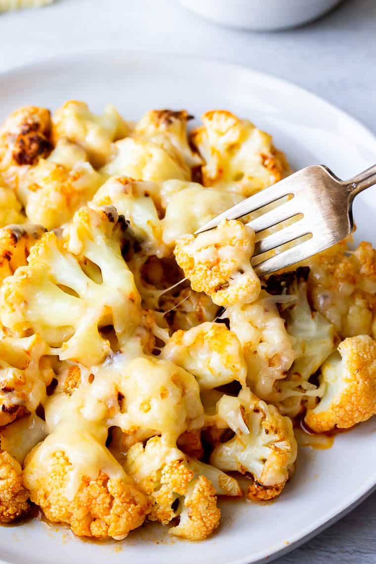 A buffalo cauliflower bite being lifted up on a fork with a cheese pull over a white background