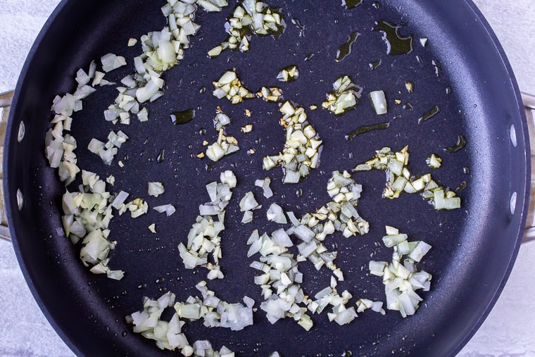 Onion and garlic cooking in a black skillet over a white background
