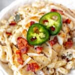 Close up of jalapeno popper chicken pasta in a white bowl with text overlay.