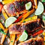 Overhead of sheet pan salmon fajitas with peppers and onion on a baking sheet with limes and cilantro