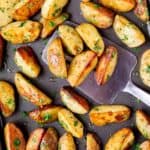Close up of Oven Roasted Potato Wedges on a baking tray with a metal spatula scooping some up