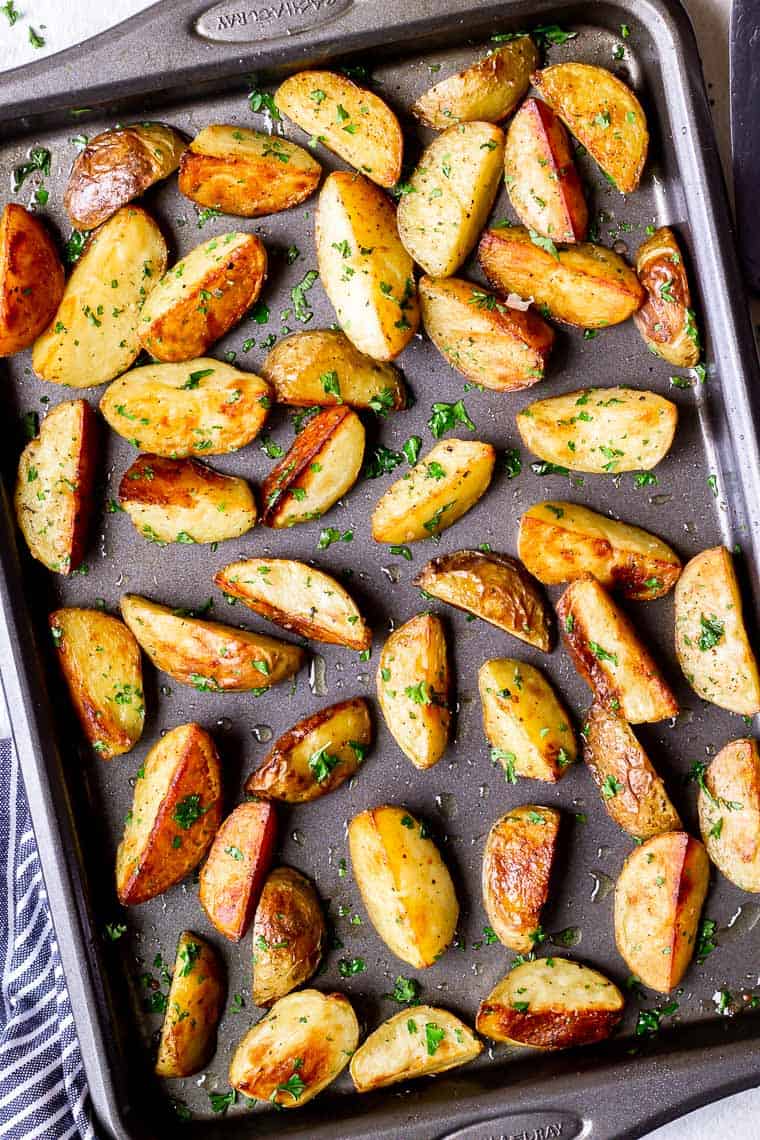 Oven Roasted Potato Wedges on a baking sheet with a blue and white striped towel on one side and minced parsley next to it