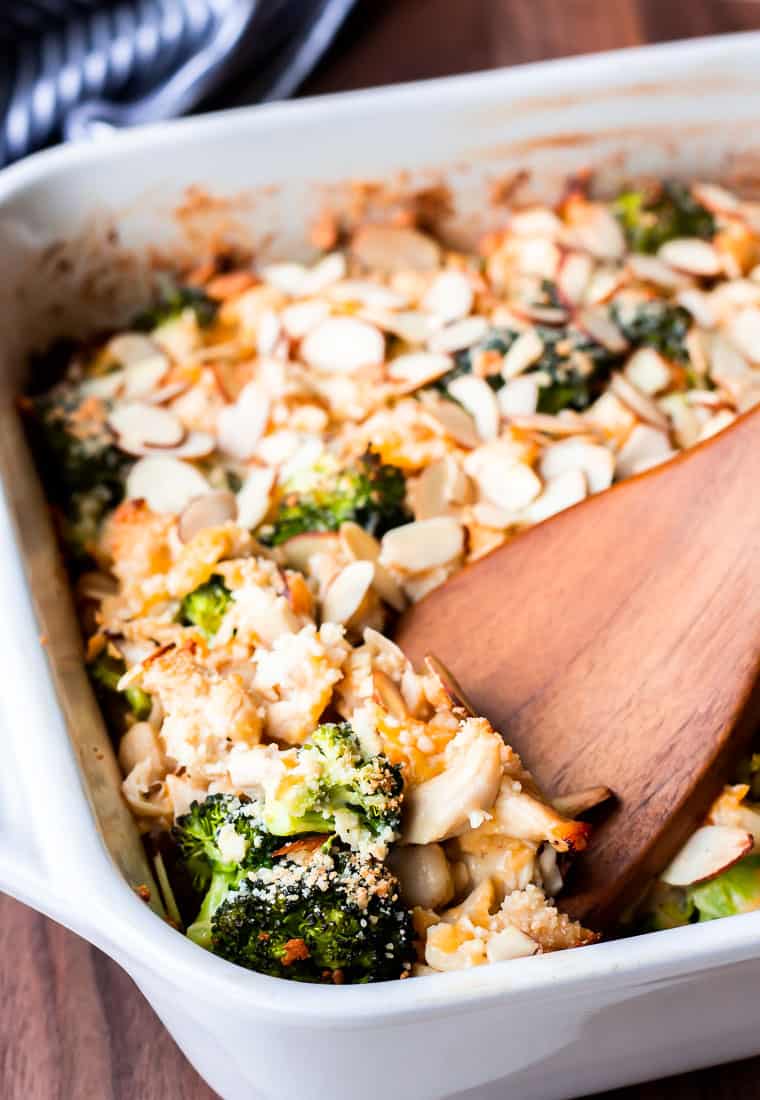 A scoop of broccoli chicken bake being listed up in the casserole dish with a wood turner over a wood board
