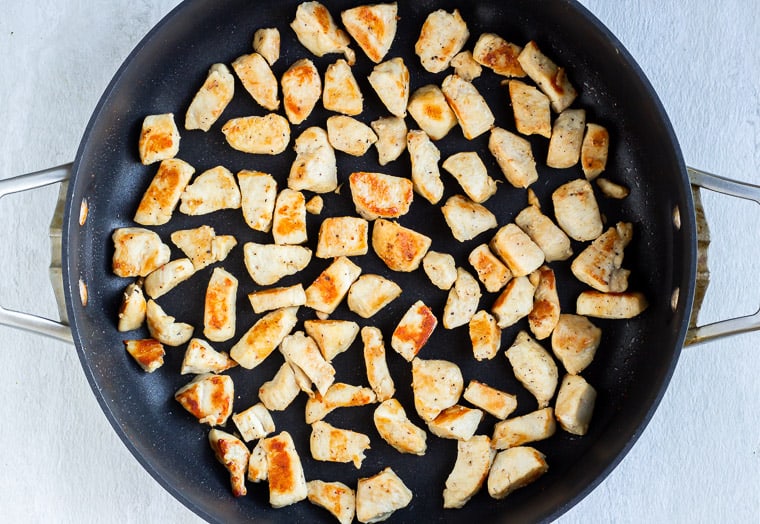 Chunks of chicken cooking in a black skillet over a white background