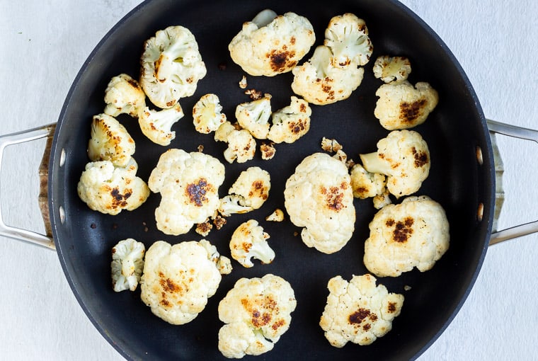 Cauliflower florets cooking in a black skillet over a white background