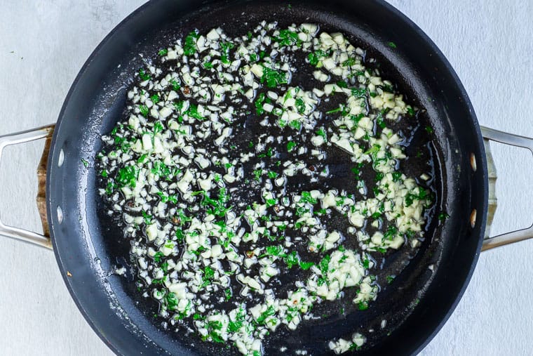Garlic and Parsley cooking in a black skillet over a white background