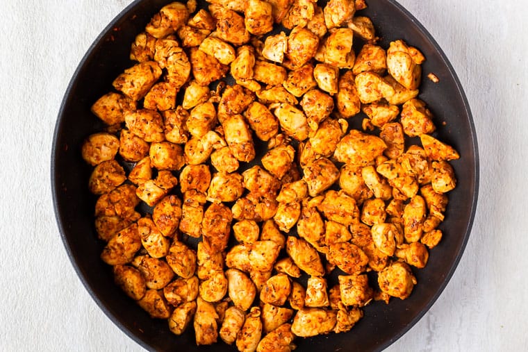 Cubed chicken with cajun seasoning cooking in a large black skillet over a white background