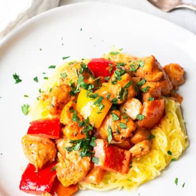A white plate of Keto Creamy Cajun Chicken and peppers over a white background with a white napkin and fork