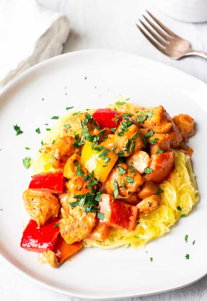 A white plate of Keto Creamy Cajun Chicken and peppers over a white background with a white napkin and fork