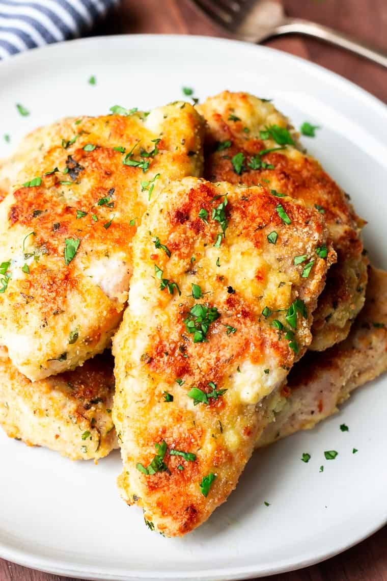 Close up of Parmesan Crusted Turkey Cutlets on a white plate on a wood table with a fork and blue and whit towel