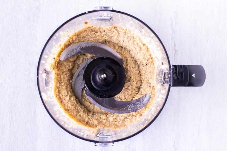 Cauliflower Hummus blended in a food processor over a white background