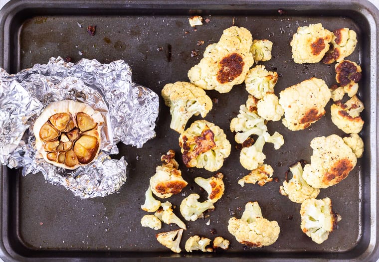 Roasted garlic and roasted cauliflower on separate sides of a baking sheet