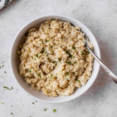 Overhead view of coconut cauliflower rice in a white bowl with a fork in it.