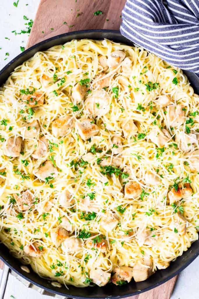 overhead of creamy garlic chicken pasta in a skillet over a wood board with a blue and white towel wrapped around the handle