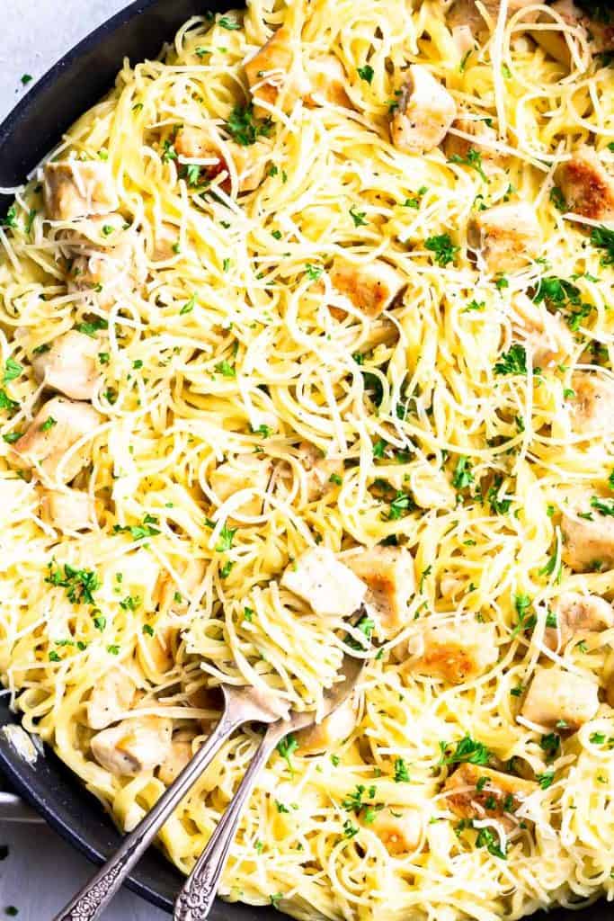 close up of garlic chicken pasta in a skillet with some wrapped around a fork with a spoon under it