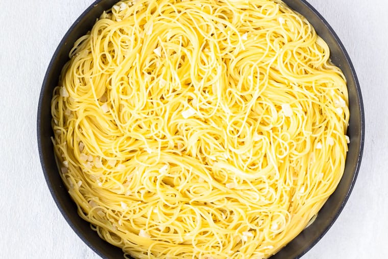 Cooked angel hair pasta in a skillet over a white background