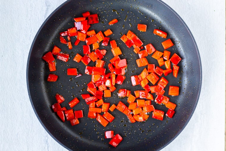 Diced red peppers cooking in a black skillet over a white background