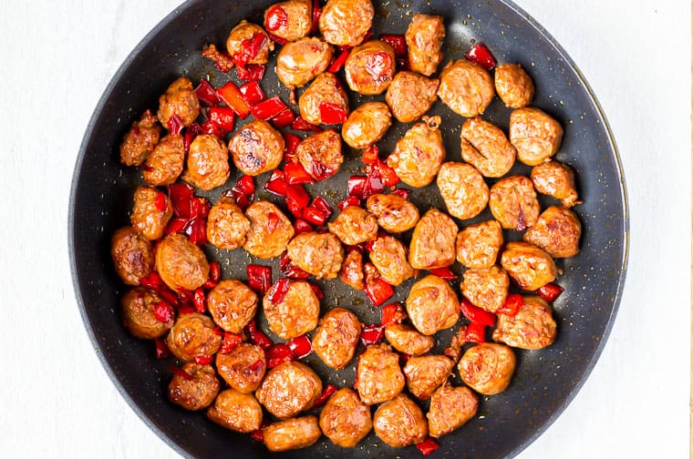 Sausage sliced and diced red pepper cooking in a black skillet over a white background