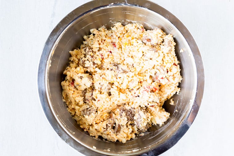 Hot sausage, cheese, and cauliflower rice mixture in a silver bowl over a white background