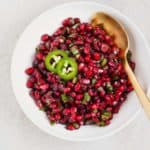 Pomegranate salsa in a white bowl with a gold spoon over a white table