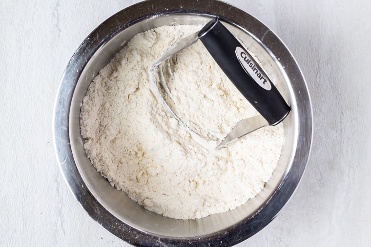 Flour with butter cut in and a pastry cutter in a silver bowl over a white background