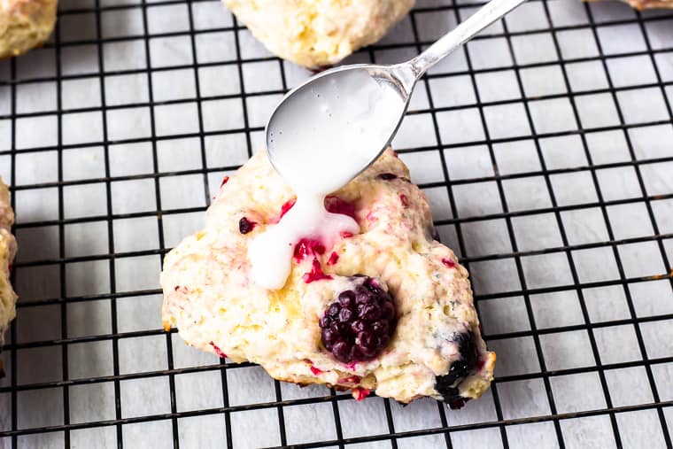 Vanilla Glaze being drizzled over a mixed berry scone on a wire rack