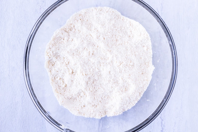 Dry ingredients for scones in a large glass bowl over a white background