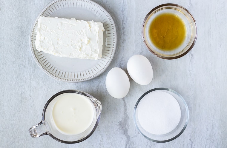 Ingredients for a crustless cheesecake in glass bowls on a white background