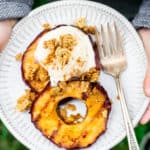 Close up of a childs hands holding a white plate with grilled apples and ice cream on it over grass