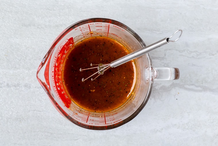 Bourbon brown sugar marinade in a measuring cup with a whisk over a white background