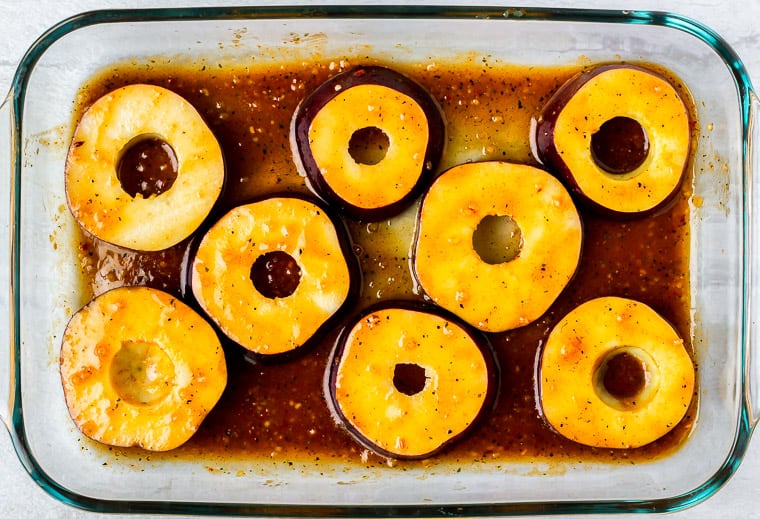 Apple slices in the brown sugar bourbon marinade in a large rectangular glass baking dish