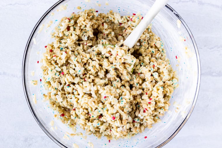 Rice krispies treats mixture with sprinkles in a glass bowl with a spatula