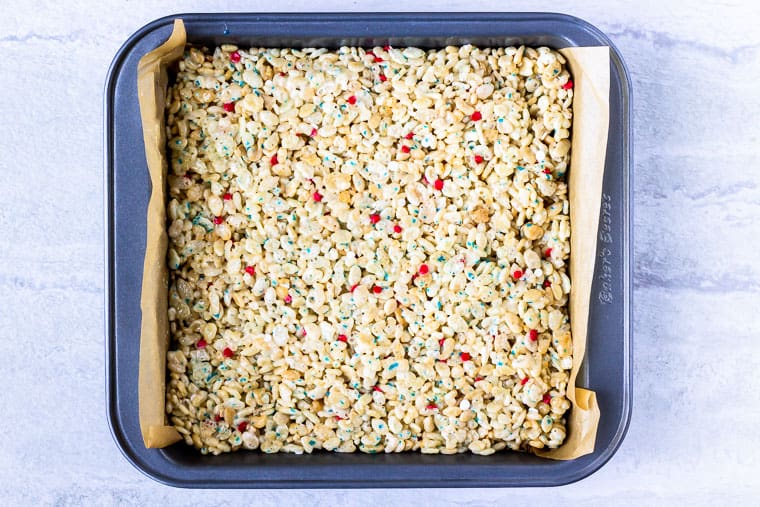 Rice krispies pressed into a square baking pan over a white background