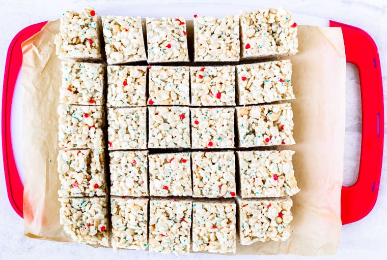 Rice krispies treats cut into 25 squares on a red and white cutting board