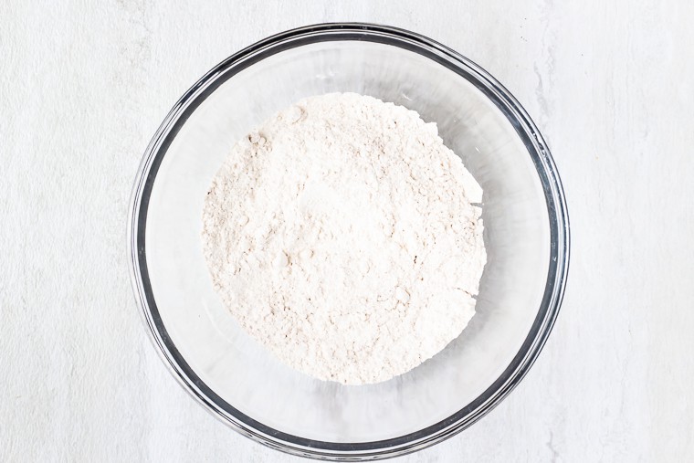 Dry ingredients for pancakes in a glass bowl on a white background