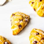 Scattered pumpkin scones on a white background with a spoon of vanilla glaze with some drizzled on the background behind them