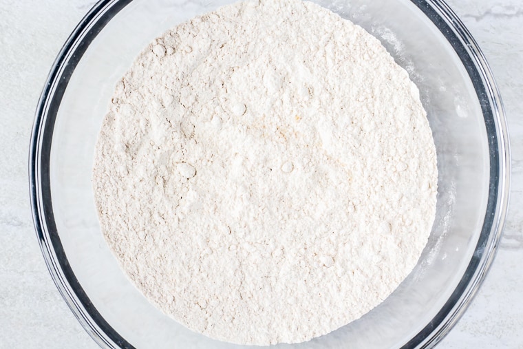 Dry ingredients for scones in a glass bowl over a white background